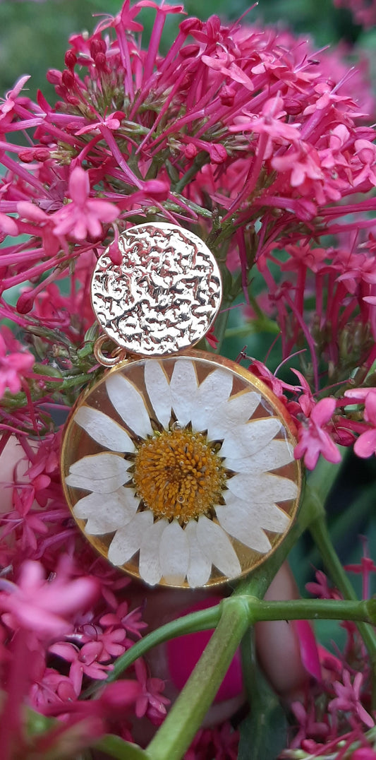 Exquisite golden earrings adorned with a real white flower on a rough, nature-inspired base